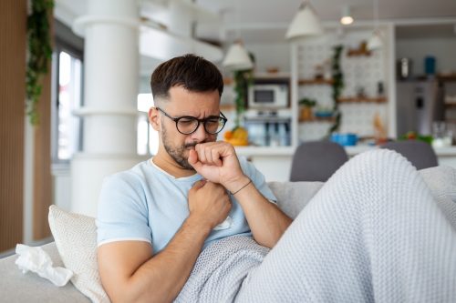 Sick man holding his chest in pain while coughing in the living room.