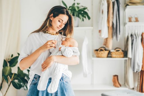 Long haired brunette chooses clothes in the wardrobe and holding little baby in arms.