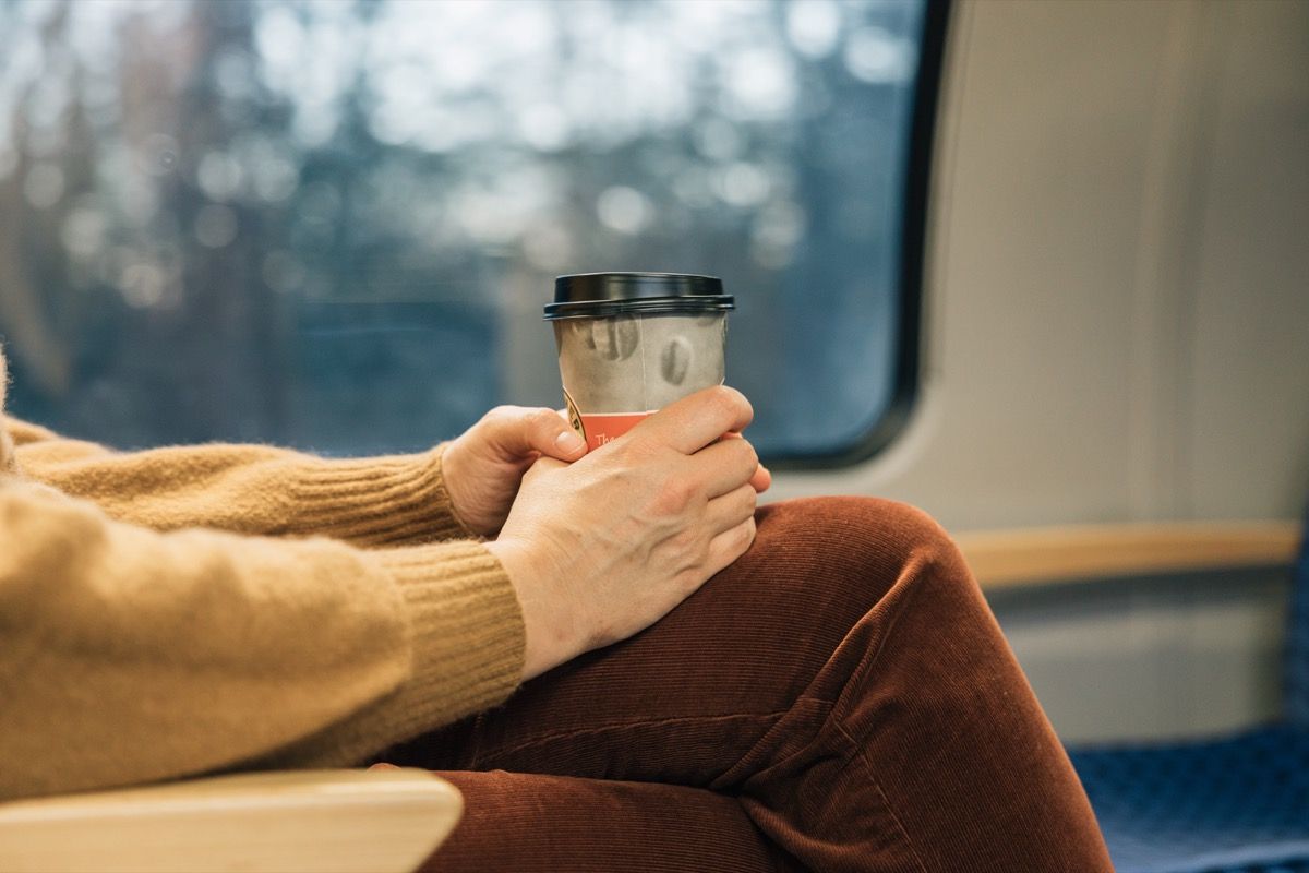 Hands of unrecognizable person holding a cup of coffee to go while traveling on a train