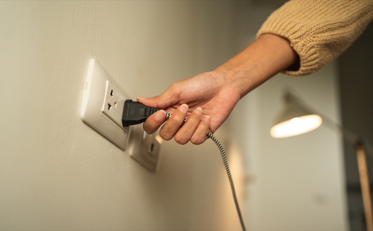 Close up woman hand put on or remove Electric plug cable in socket. Electrical equipment wires and power strips on the wall. Earth Hour saving energy.