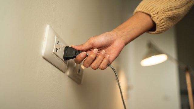 Close up woman hand put on or remove Electric plug cable in socket. Electrical equipment wires and power strips on the wall. Earth Hour saving energy.