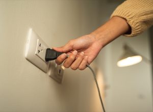 Close up woman hand put on or remove Electric plug cable in socket. Electrical equipment wires and power strips on the wall. Earth Hour saving energy.