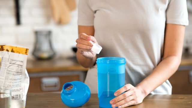 Woman's hand holding scoop while adding protein powder to protein shaker bottle