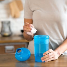 Woman's hand holding scoop while adding protein powder to protein shaker bottle