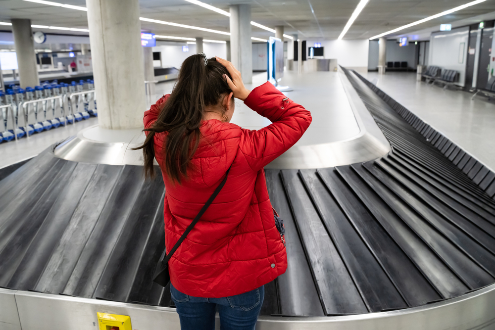 A woman standing at baggage claim with her hands on her head