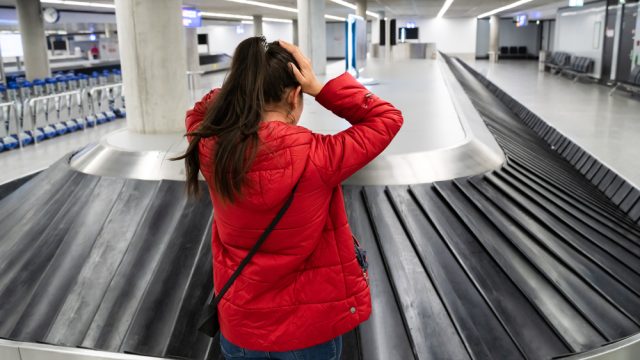 A woman standing at baggage claim with her hands on her head