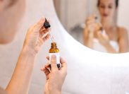 Woman in front of a mirror holding face oil for daily skincare routine in a bottle with a dropper