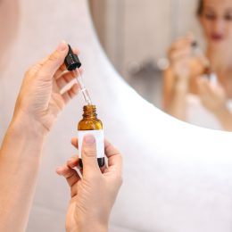 Woman in front of a mirror holding face oil for daily skincare routine in a bottle with a dropper
