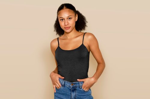 young woman wearing a black tank top and jeans against a beige background