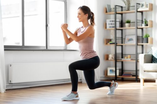 Woman in black leggings and pink tank top doing a lunge in her living room