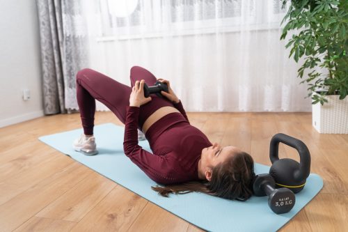 Young woman in a maroon workout outfit doing glute bridge using dumbbell on blue yoga exercise mat.