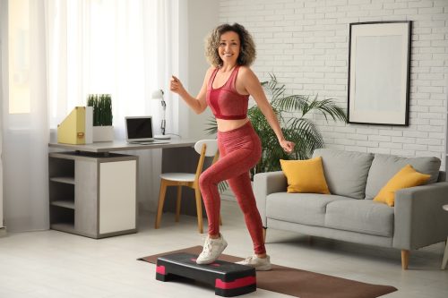 woman dressed in a red bra and leggings is exercising with a stepper at home