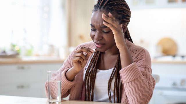 woman with a headache taking a pill with a glass of water