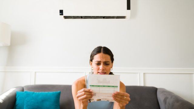 Worried young woman looking stressed while receiving the electricity bill after using the air conditioner at home