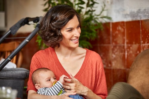 Happy mother in an orange shirt carrying baby while sitting in restaurant