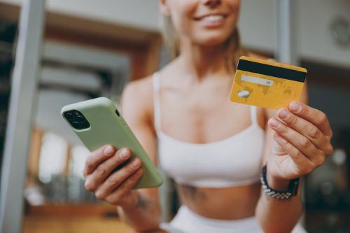 Cropped image of a woman in a white workout outfit ordering something with her credit card on her phone