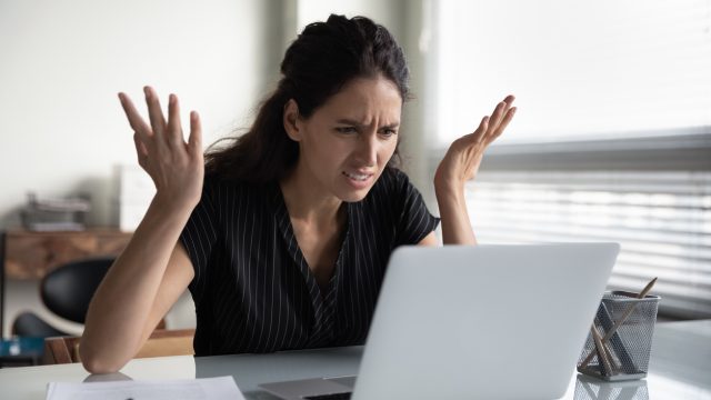 A woman looking at her laptop with a confused and angry expression