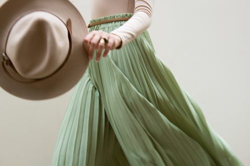 cropped image of a woman wearing light green pleated pants, holding a beige cowboy hat