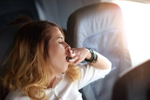 portrait of sleepy business woman feeling exhausted and yawning, photo taken inside the airplane.