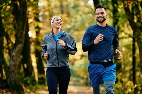 Happy couple of athlete running in the park in autumn. Copy space.