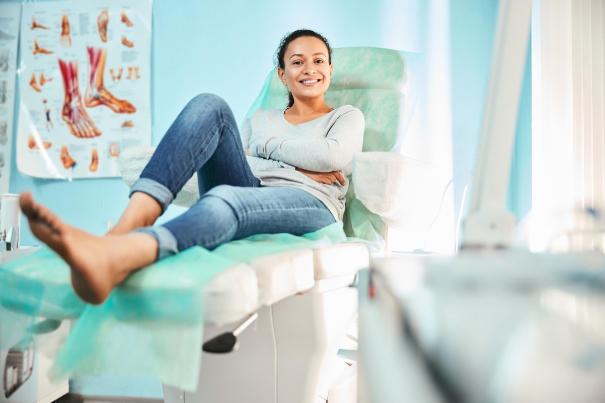 Full length portrait of happy cheerful female in casual clothes sitting on the medical chair and waiting for pedicure procedure in beauty clinic