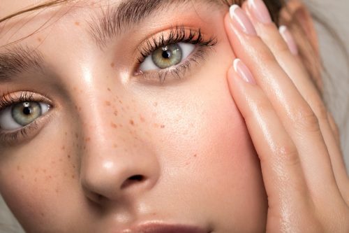 Closeup studio shot of a beautiful young woman with freckles posing against a grey background