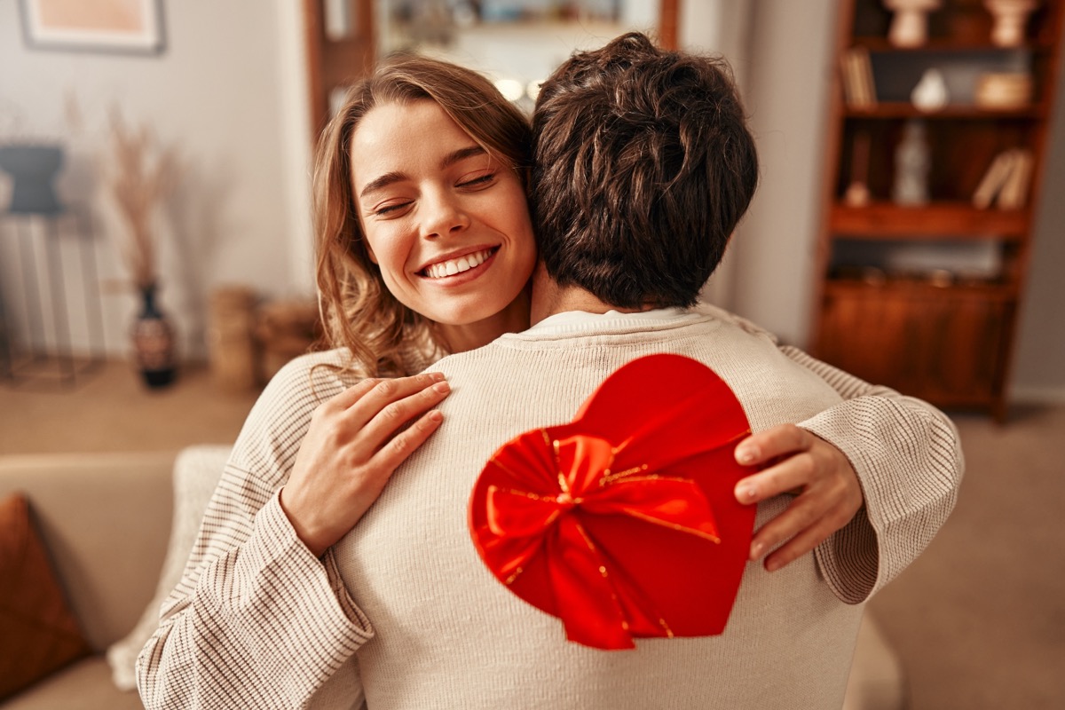 A man gives a heart-shaped gift box to his beloved woman in the living room at home.