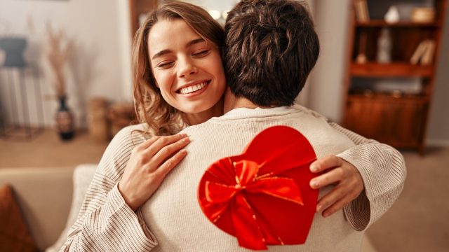 A man gives a heart-shaped gift box to his beloved woman in the living room at home.