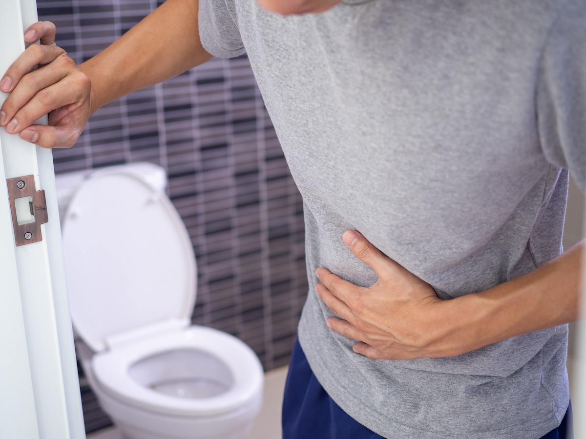 Man with a stomach ache holding the bathroom door and clutching his stomach