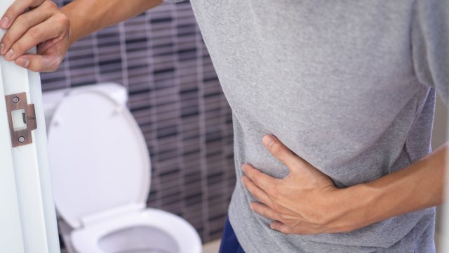 Man with a stomach ache holding the bathroom door and clutching his stomach