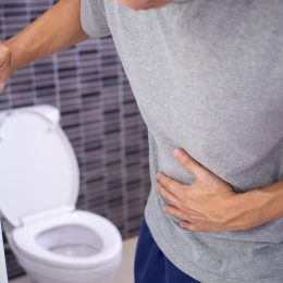 Man with a stomach ache holding the bathroom door and clutching his stomach