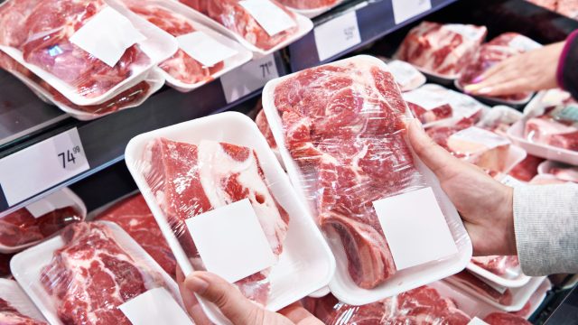 Hands of a person comparing packaged red meat in the grocery store