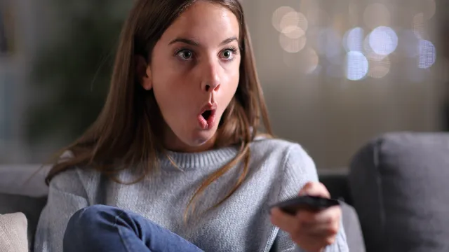 Surprised woman watching tv sitting on a couch at home in the night