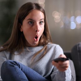 Surprised woman watching tv sitting on a couch at home in the night