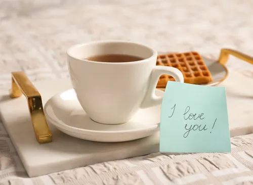 Paper note I Love You near cup of morning drink and waffle on bed. Romantic breakfast