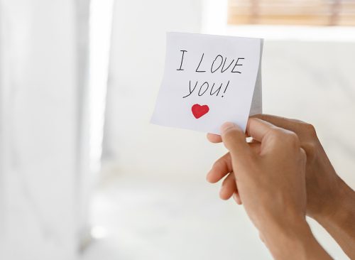 Woman Putting Sticky Note With I Love You Text On Mirror, Closeup Shot Of Female Hand Sticking Paper, Leaving Handwritten Romantic Messase With Drawn Heart, Cropped Image