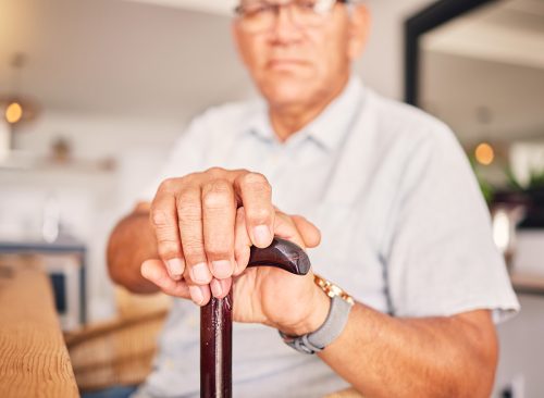 Hands, serious and portrait of a man with a cane for medical help, senior support and health. Sad, house and an elderly person with a disability in the living room with a walking stick closeup