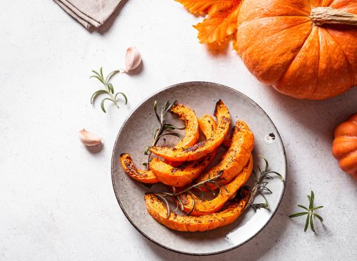 Grilled pumpkin slices with garlic and herbs on white background, copy space. Oven baked pumpkin, seasonal autumn side dish or vegan meal.