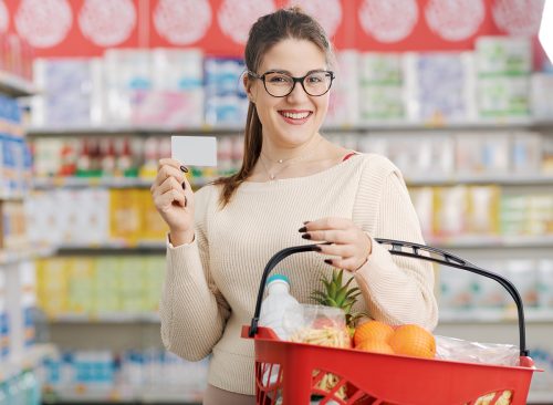 Smiling customer holding a shopping basket and showing a blank loyalty card at the supermarket, grocery loyalty program and discounts concept