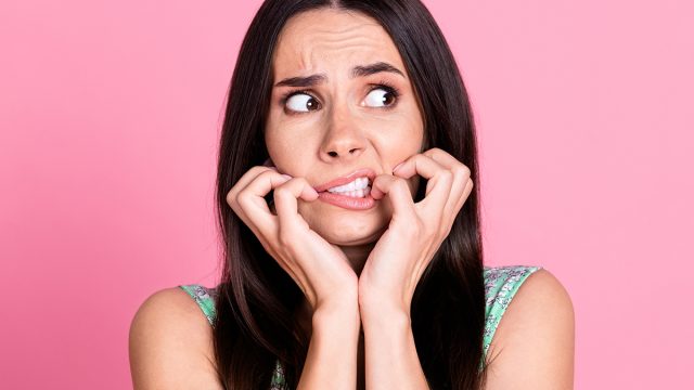 Photo of anxious embarrassed woman wear trendy clothes biting fingernails empty space isolated on pink color background