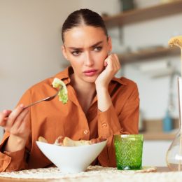 upset-looking woman sitting alone at table eating caesar salad