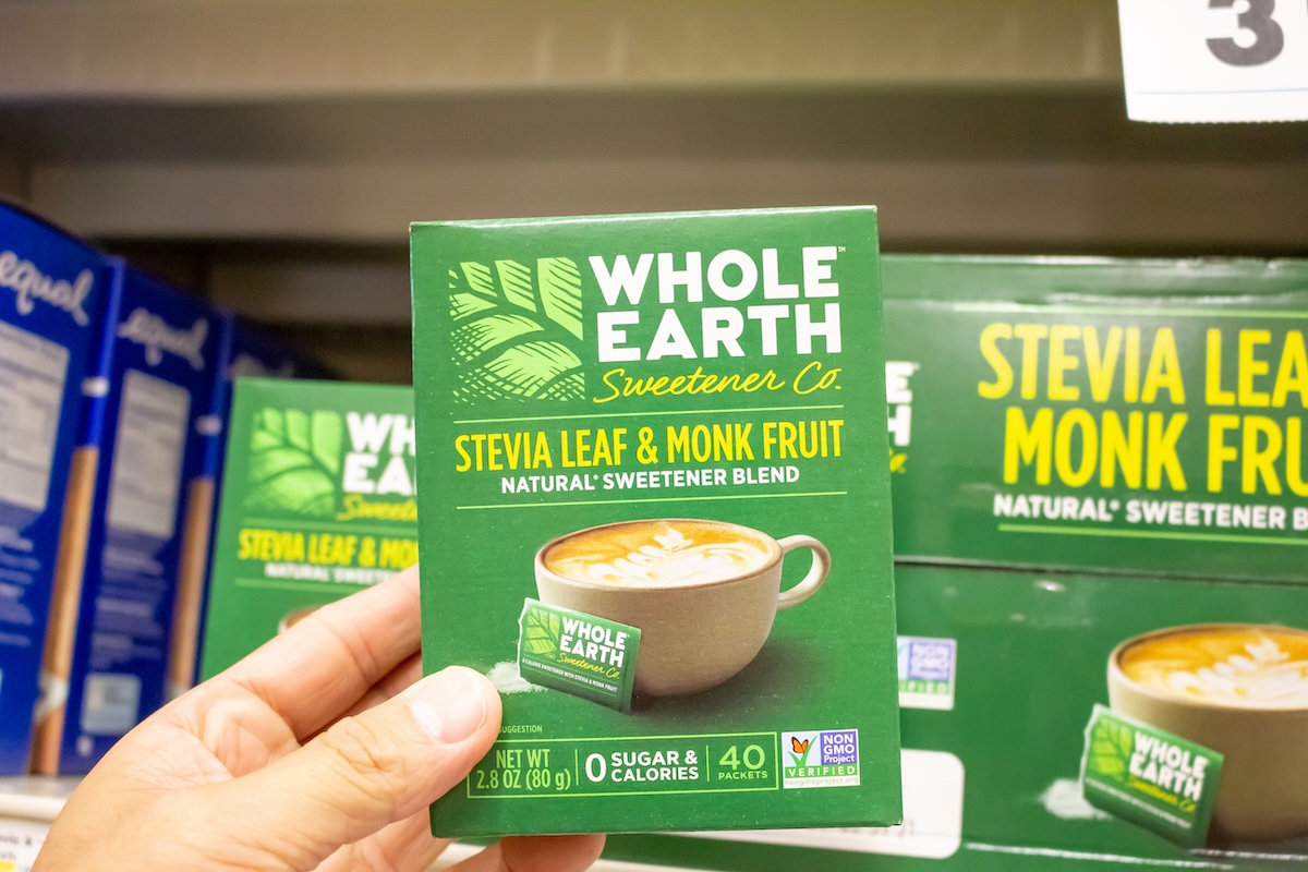A view of a hand holding a package of Whole Earth Sweetener Company Stevia Leaf and Monk Fruit Natural Sweetener Blend at a local grocery store.