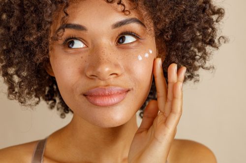 Closeup of a young woman with freckles using face cream