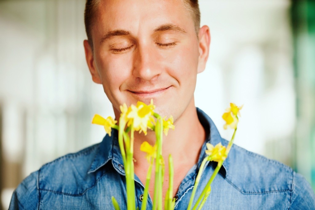 man in a denim shirt smelling yellow flowers