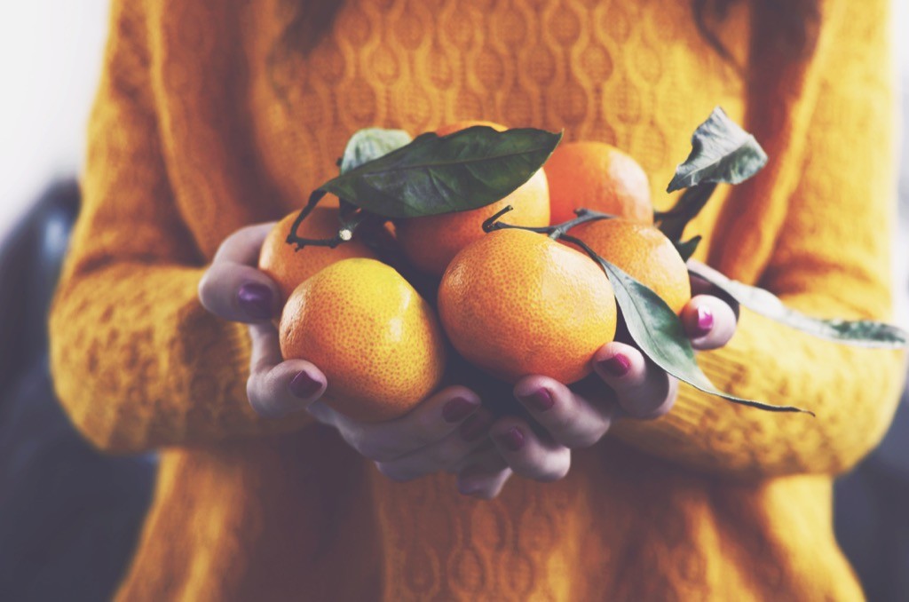 woman in a yellow sweater holding clementines