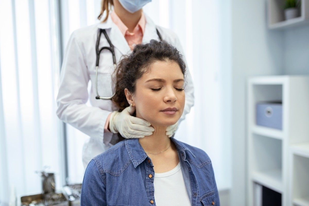 Endocrinologist examining throat of young woman in clinic.