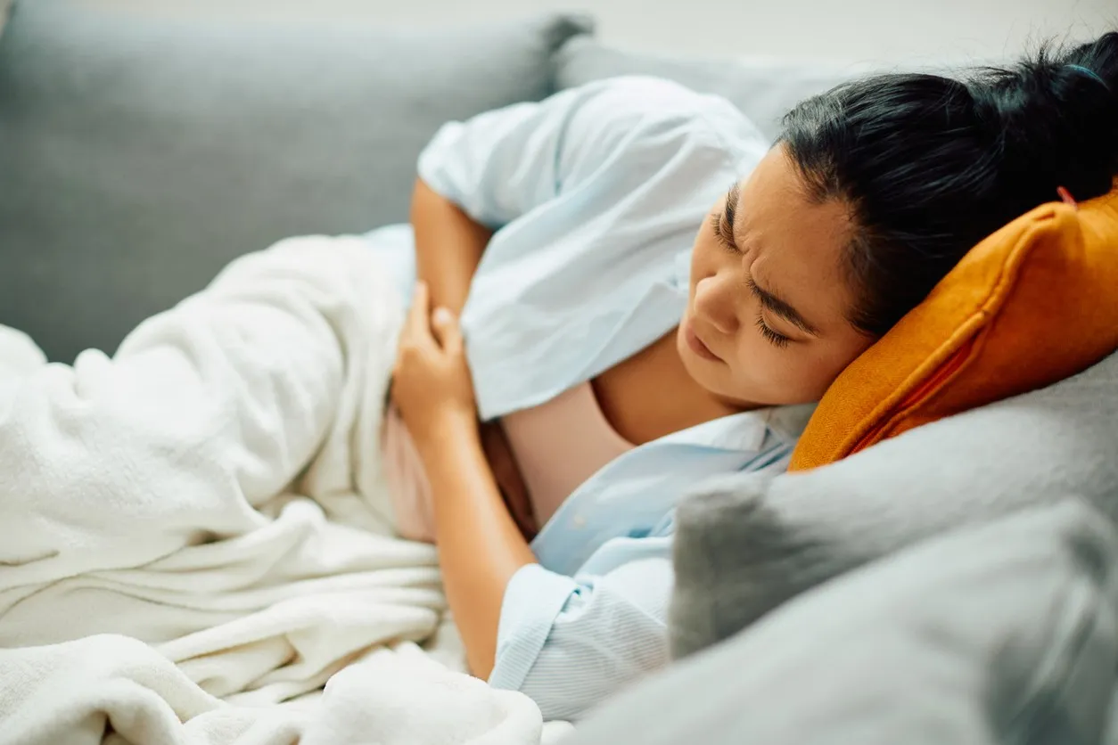A young woman lying on the couch while holding her stomach with food poisoning symptoms or a stomach ache