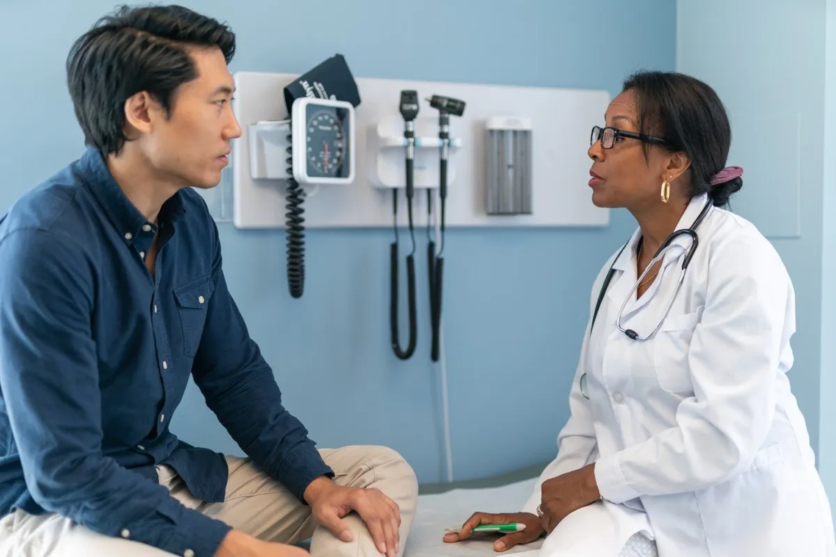 Male patient sitting on an exam table speaking to a female doctor
