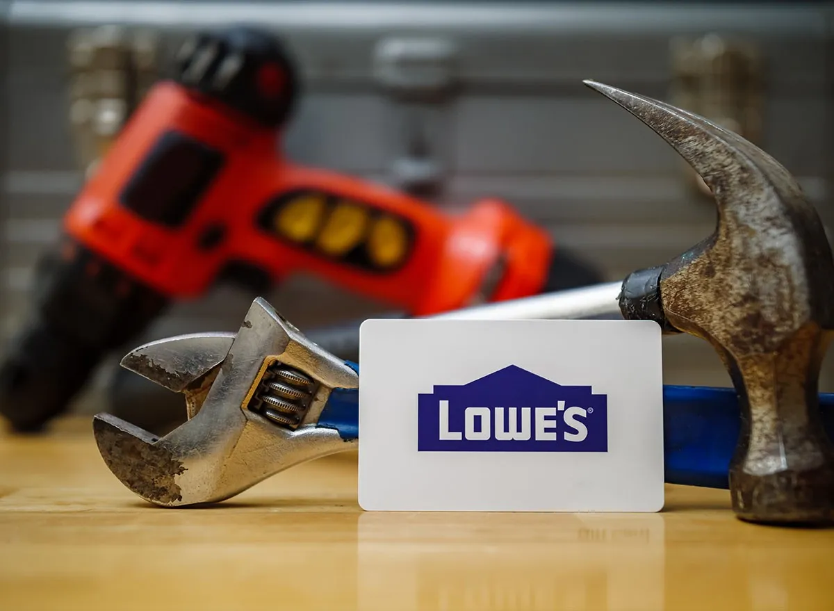 A Lowe's card in front of various tools on a wood table