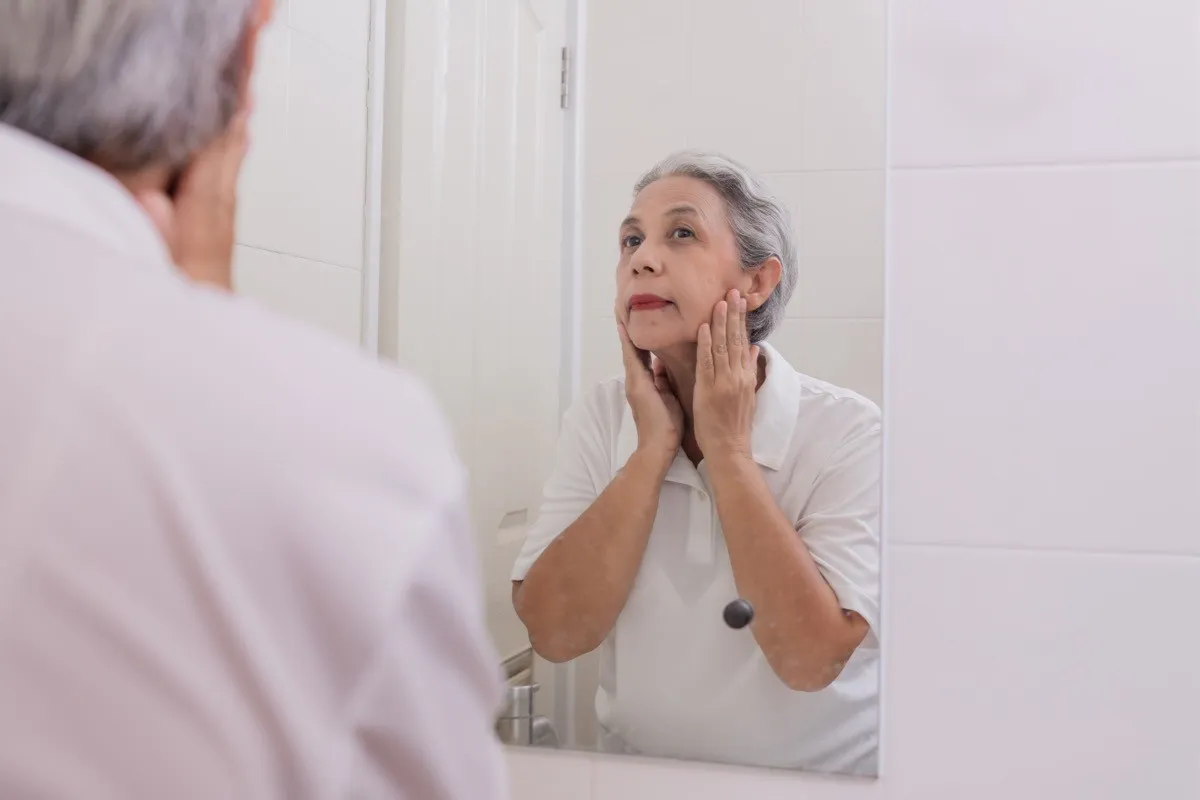 older woman looking at her skin in the mirror